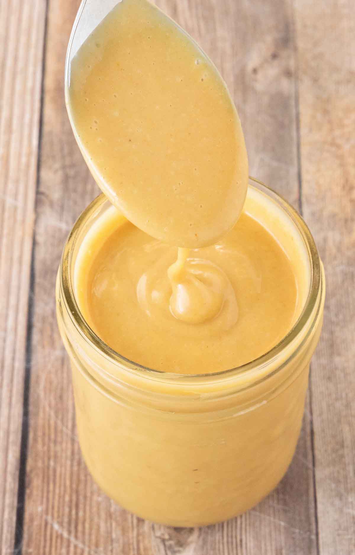 The finished Chick-fil-A sauce recipe in glass jar with a spoon of sauce coming out.