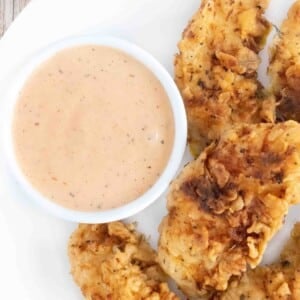 Chicken dipping sauce with chicken tenders on a white plate.