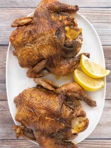 Two roasted Cornish hens on a white platter.