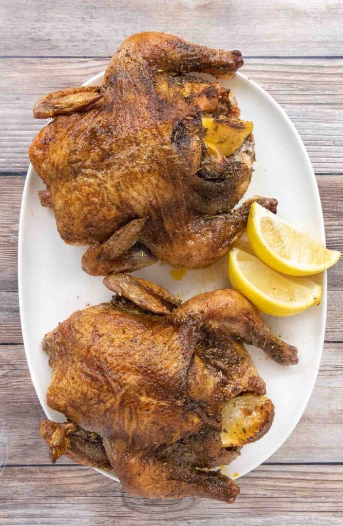 Two roasted Cornish hens on a white platter.