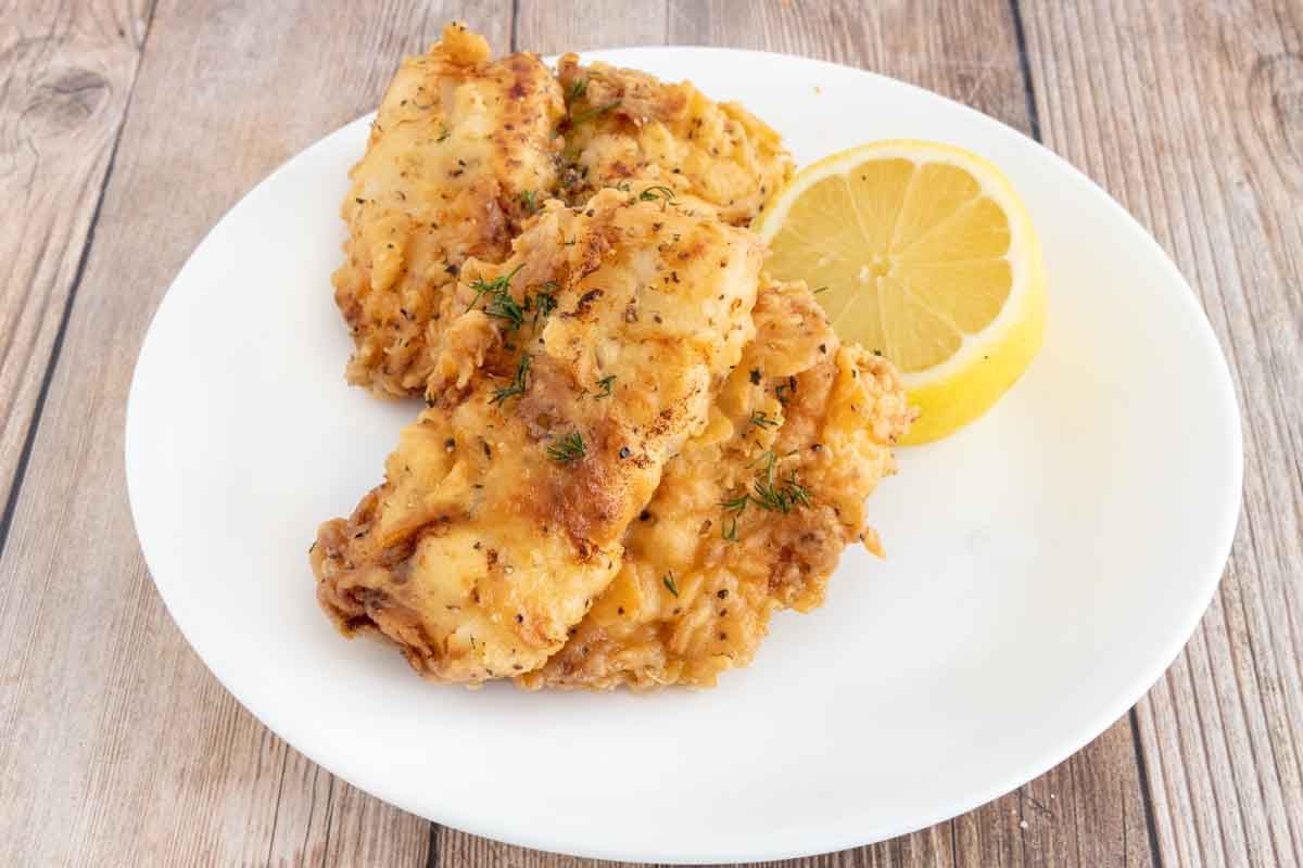 Fried walleye on a white plate with half a lemon.