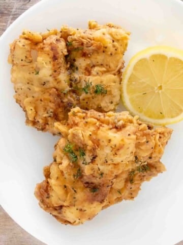 Fried walleye on a white plate with half a lemon.