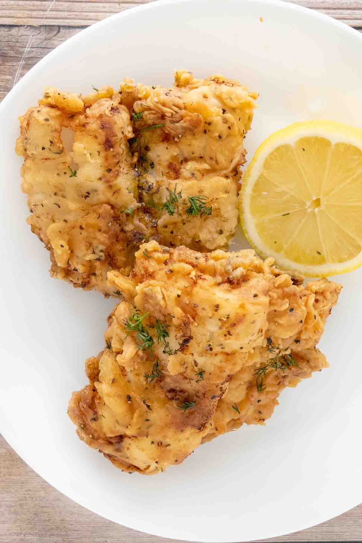 Fried walleye on a white plate with half a lemon.