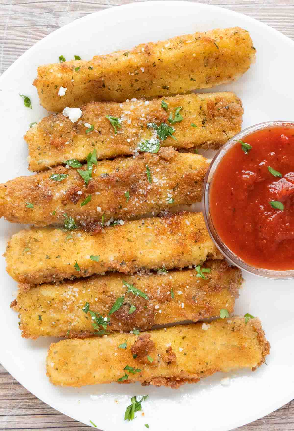 Mozzarella sticks with marinara sauce on a white plate.