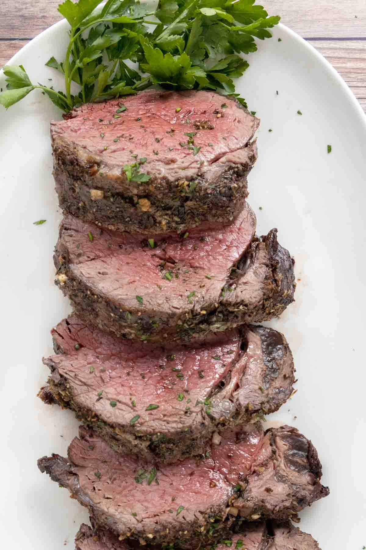 Sliced beef tenderloin recipe is served on a white platter.