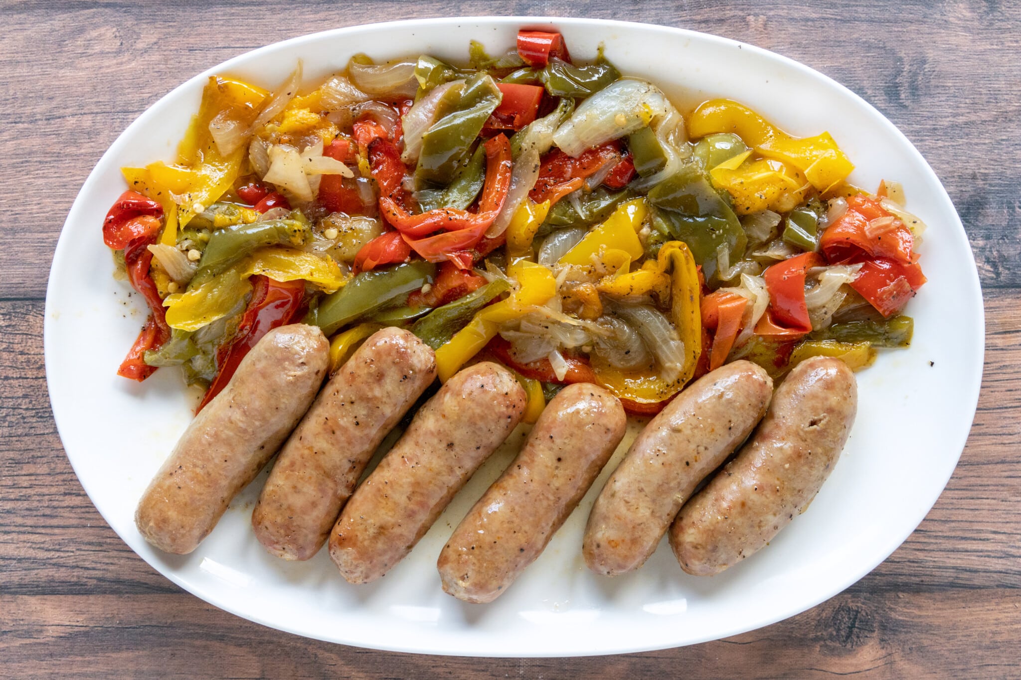 Italian sausage, peppers, and onions on a white platter.