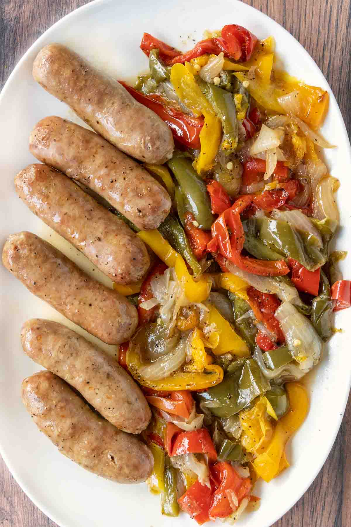 Italian sausage, peppers, and onions on a white platter.