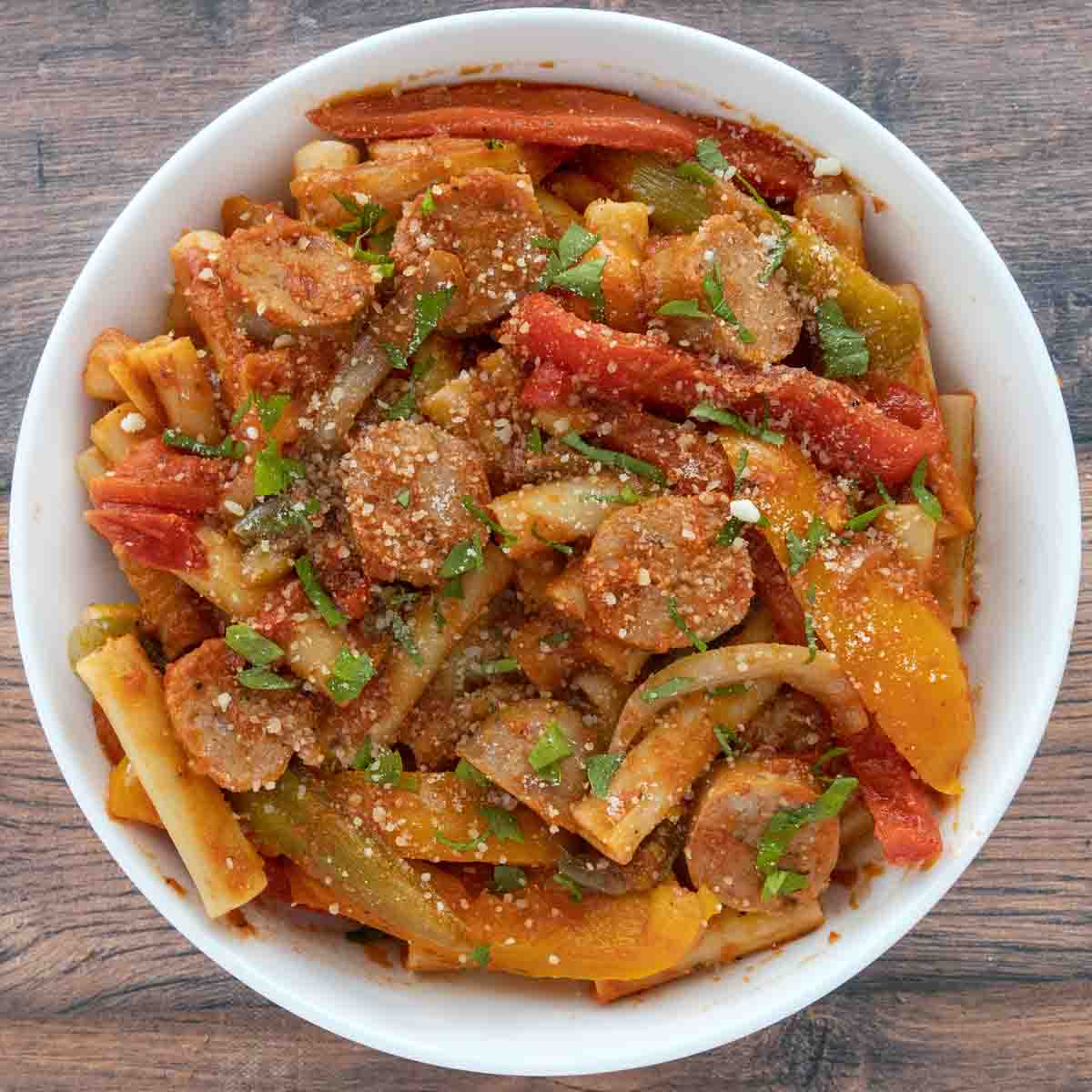 Sausage, peppers and onions with pasta in a white bowl.