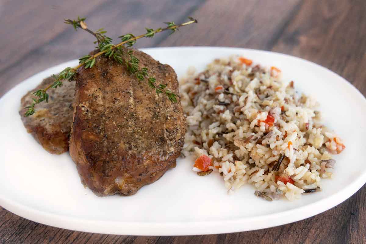 Smoked pork chops on a white plate with wild rice.