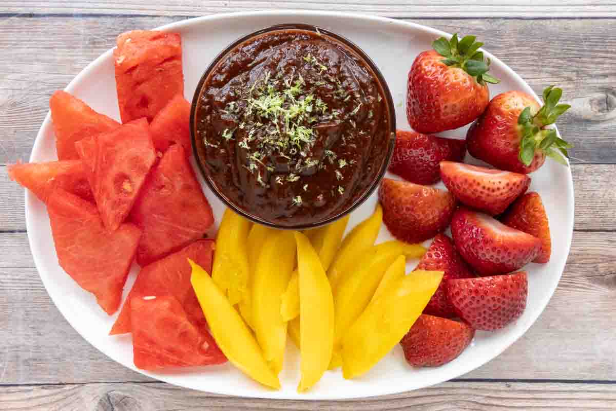 Chamoy sauce with fresh fruit on a white platter.