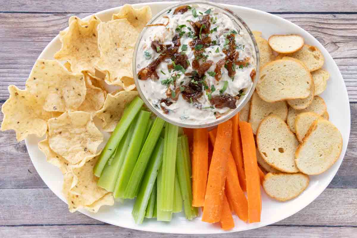 French onion dip with chips and vegetables on a while platter.