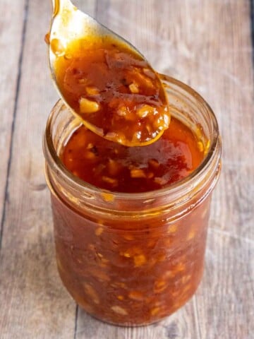 Honey sriracha sauce in a glass jar with a spoon coming out.