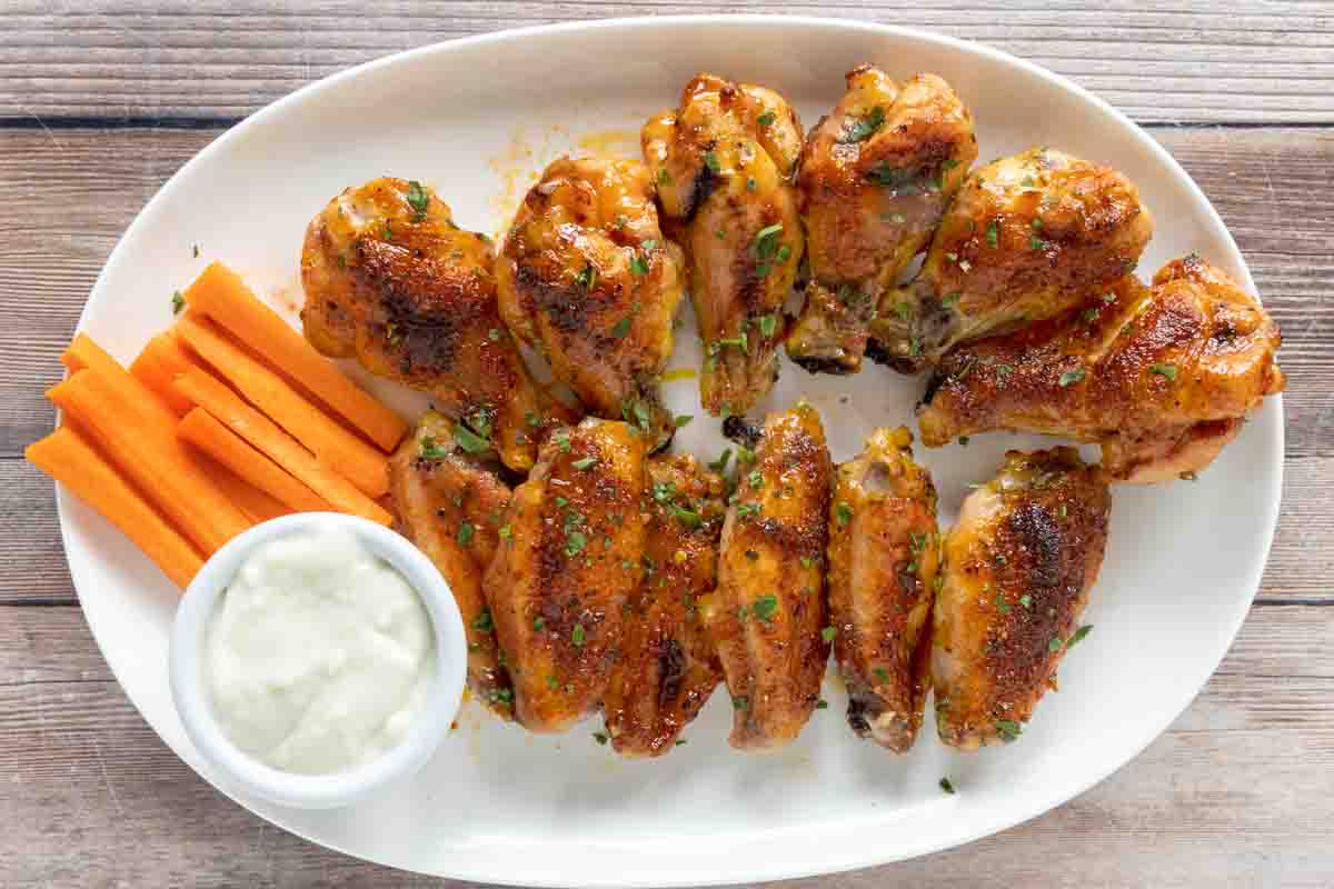 Honey Sriracha Chicken Wings with carrot sticks and ranch dressing on a white platter.