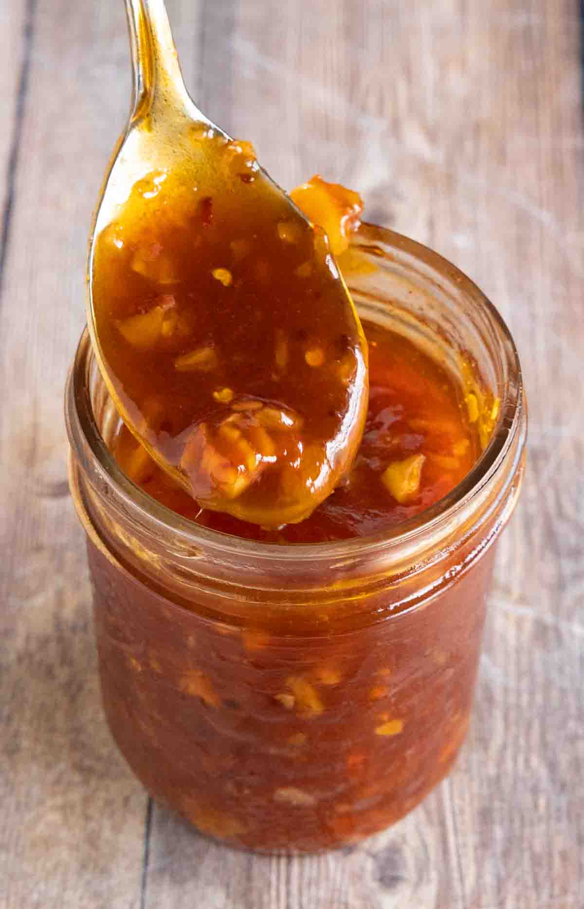 Honey sriracha sauce in a glass jar with a spoon coming out.