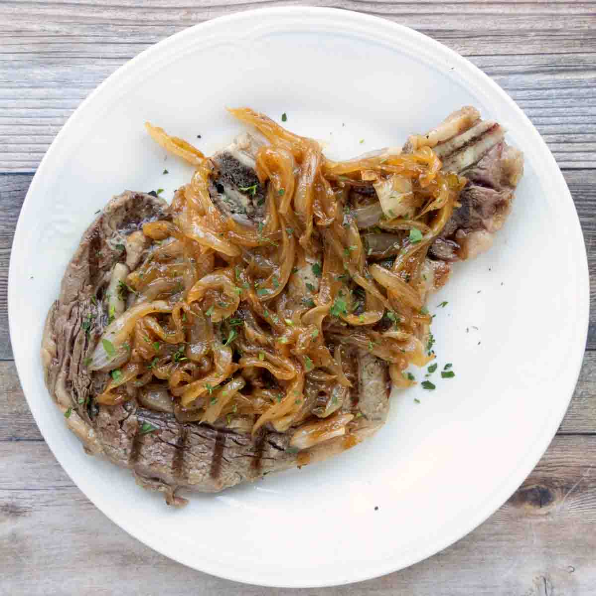 Ribeye on white plate topped with caramelized onions.