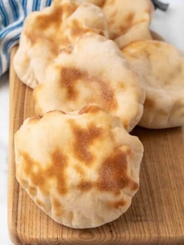 Pita bread stacked on a wooden cutting board.