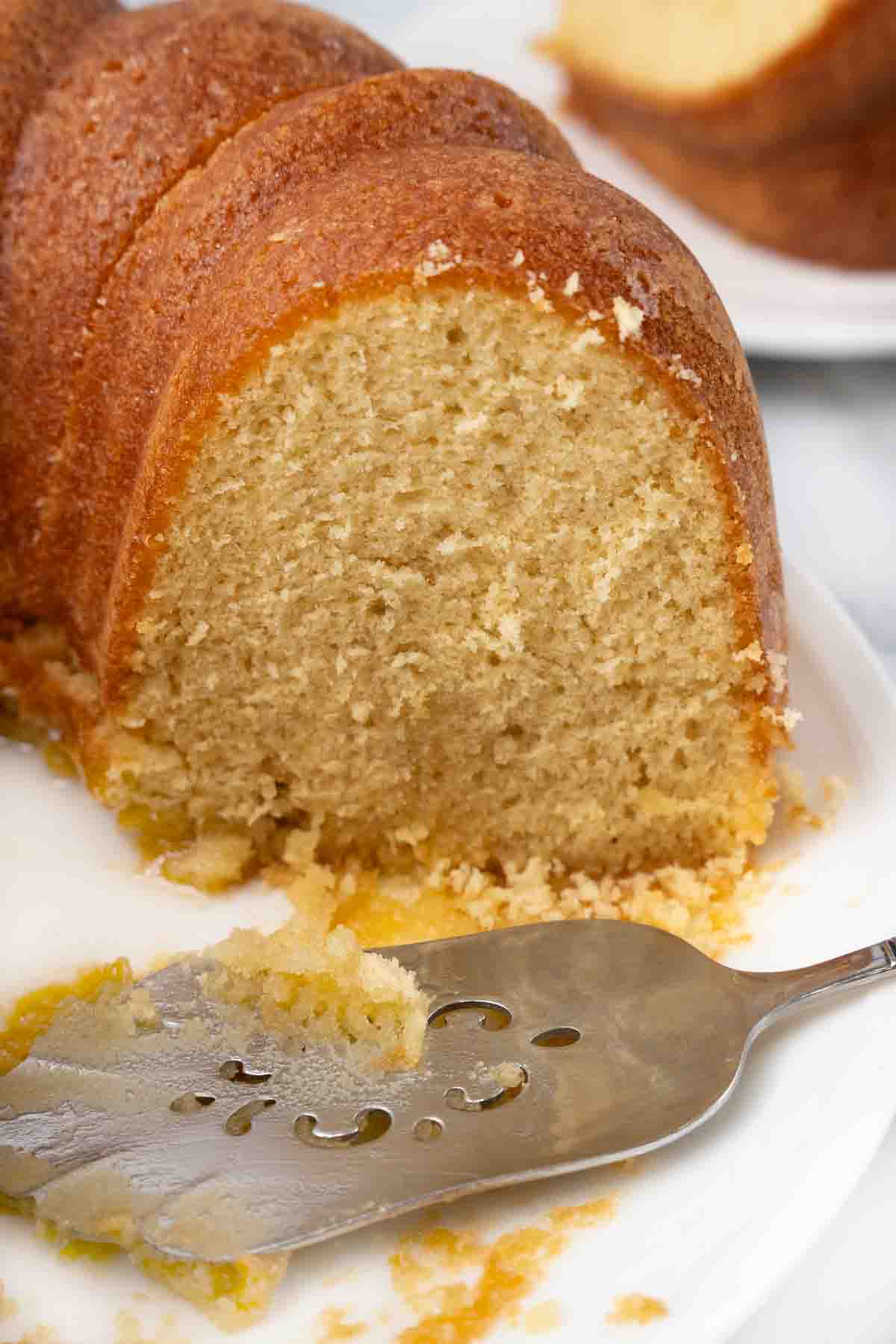 Sliced butter rum cake with cake spatula on white platter.