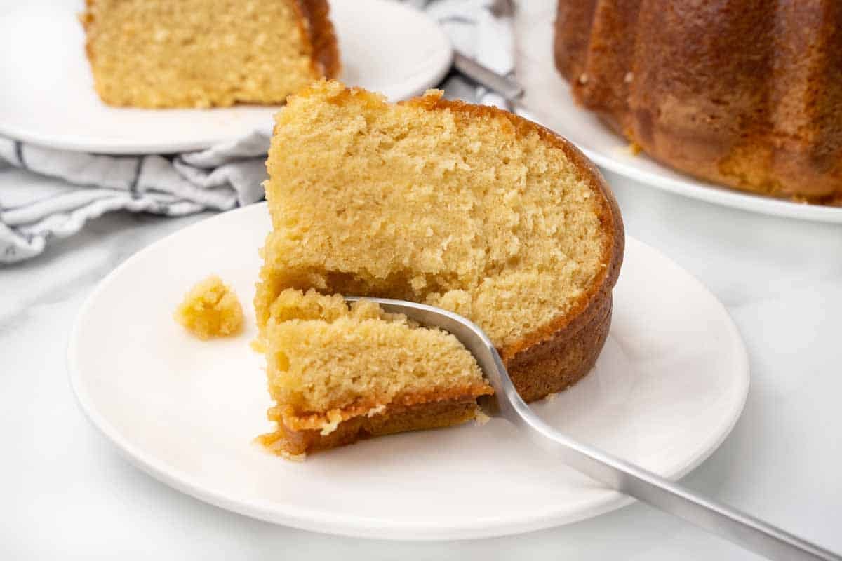 slice of butter rum cake with a fork in it on a white plate.