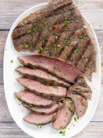 Sliced tri-tip steak on a white platter.