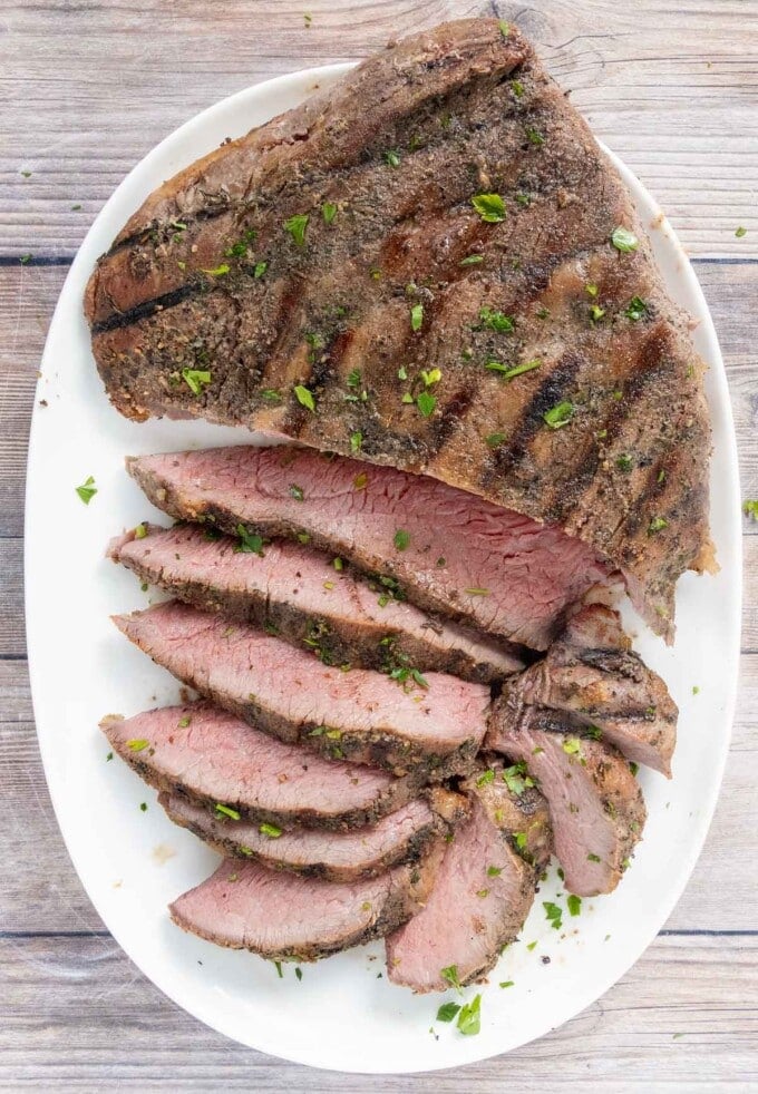 Sliced tri-tip steak on a white platter.