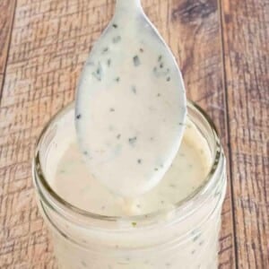 Garlic parmesan sauce in a glass jar with a spoon coming out.