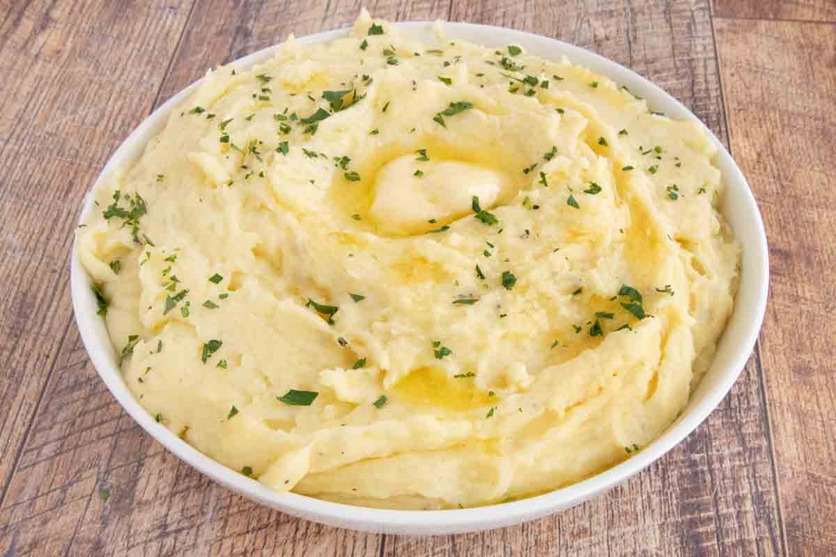 Cheesy mashed potatoes with a pat of melting butter in a white bowl.
