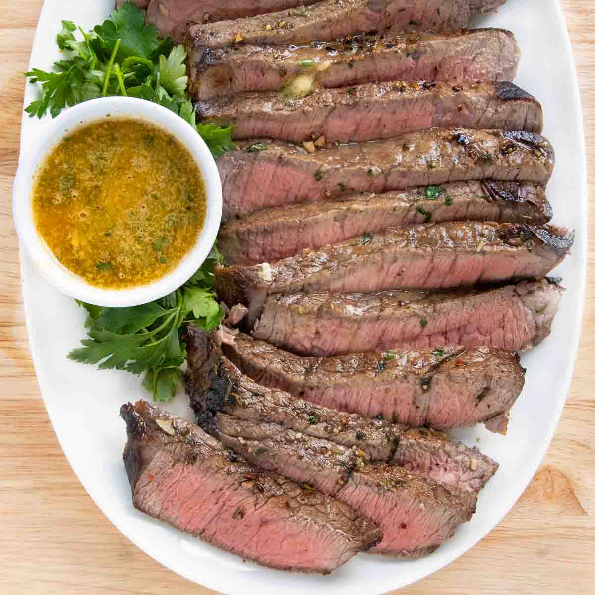 Sliced London broil on a white platter with melted butter.