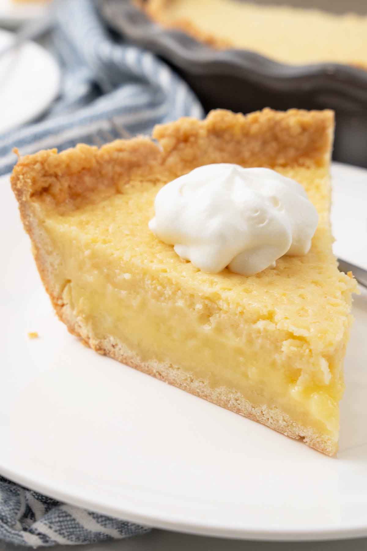 Slice of buttermilk pie with whipped cream on a white plate.