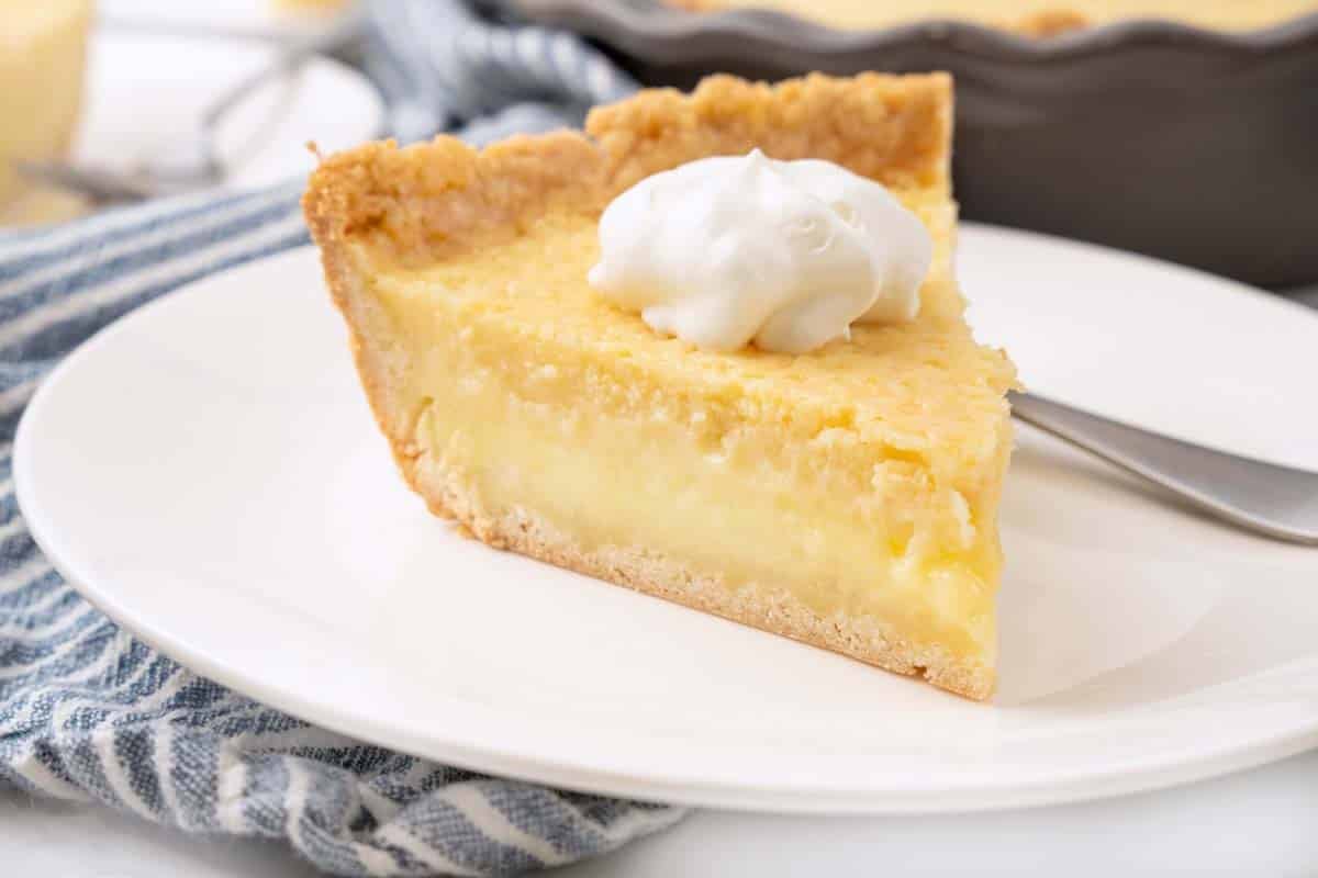 Slice of buttermilk pie with whipped cream on a white plate.