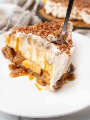 Slice of banoffee pie with a fork in it on a white plate.