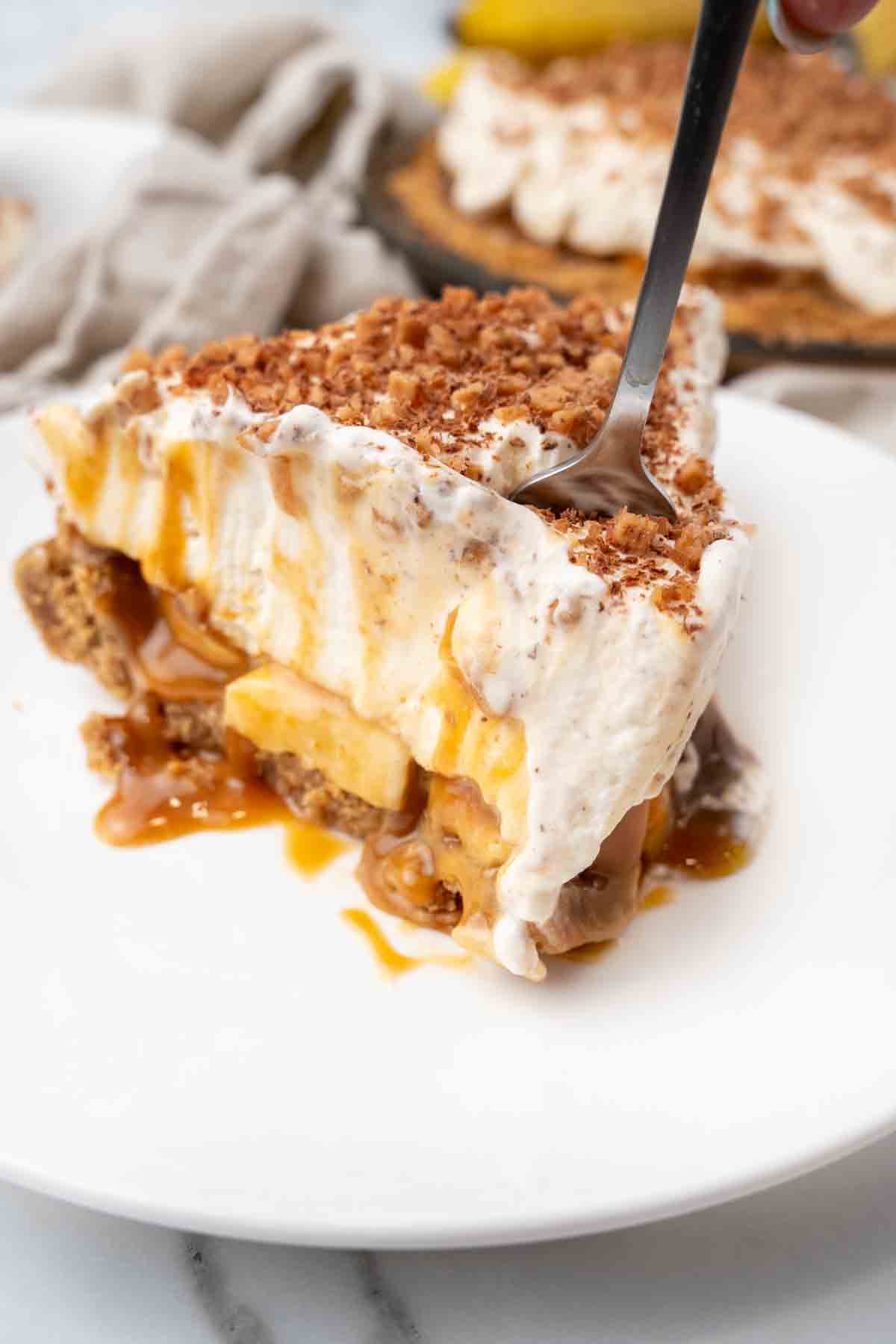 Slice of banoffee pie with a fork in it on a white plate.
