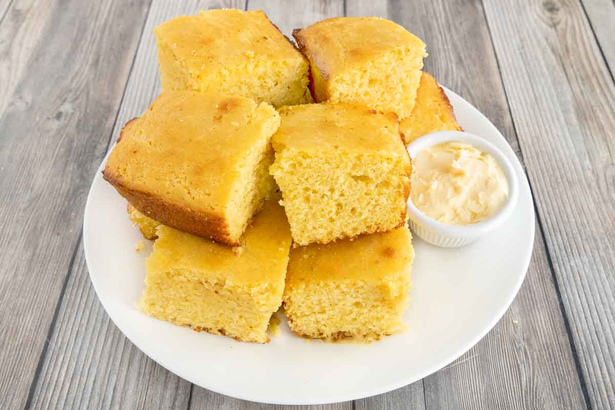Cornbread stacked on white platter with a ramekin of butter.