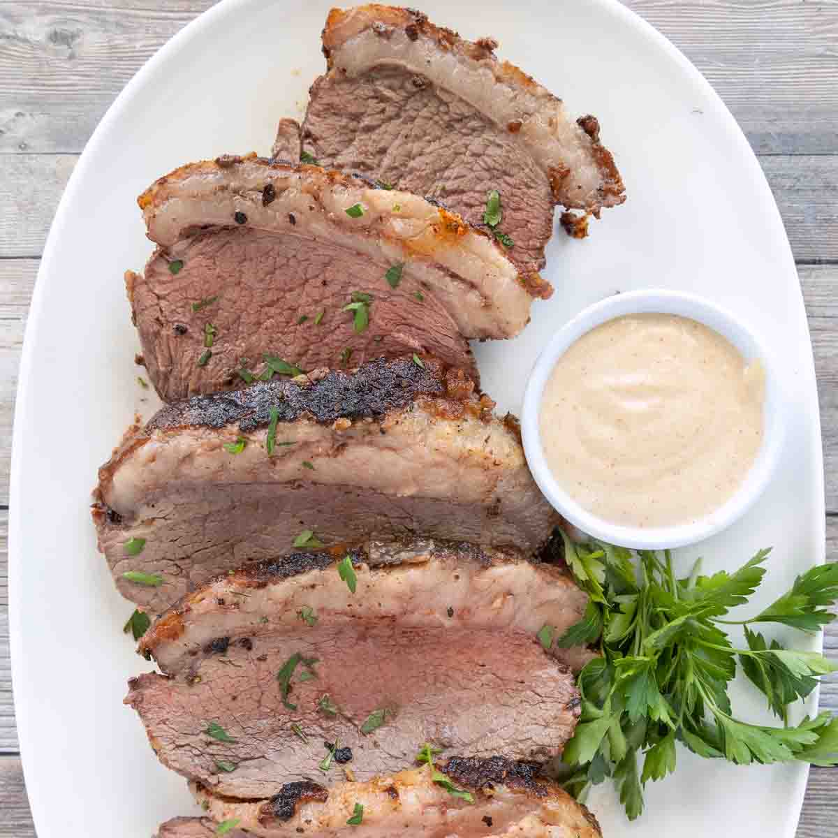 Sliced picanha roast on a white platter.