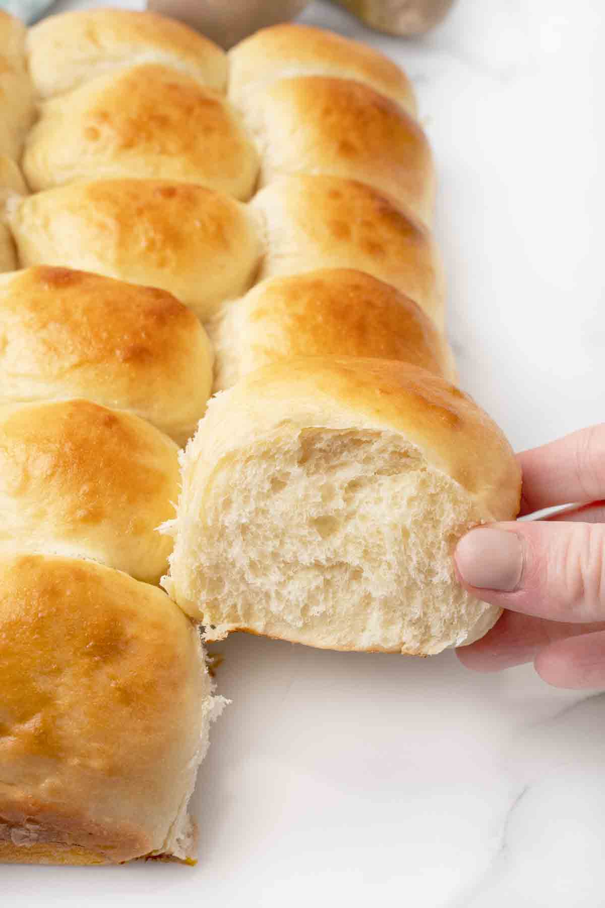 Woman's hand taking a potato dinner roll from the tray of rolls.