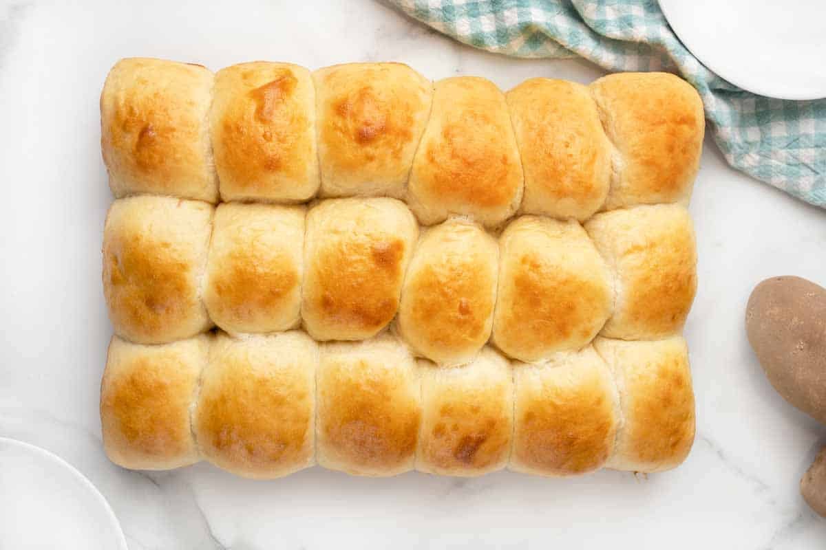 Baked potato dinner rolls all together on a white table.