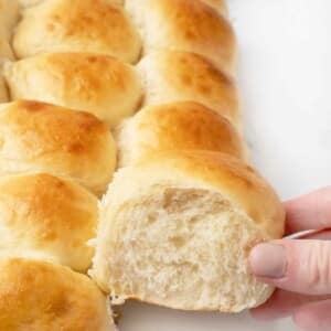 Woman's hand taking a potato dinner roll from the tray of rolls.