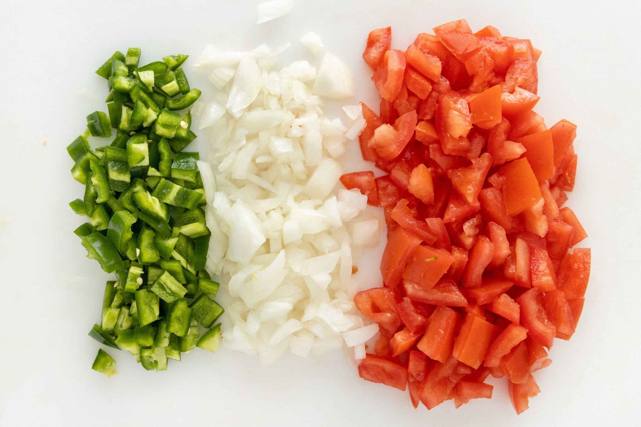 Chopped tomatoes, onions and peppers on a white cutting board.
