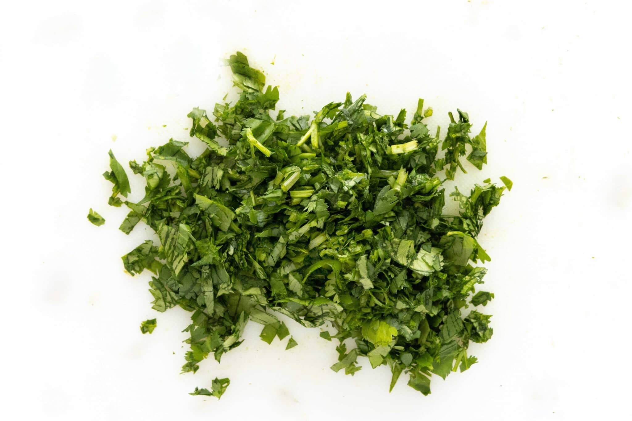 Chopped cilantro on a white cutting board.