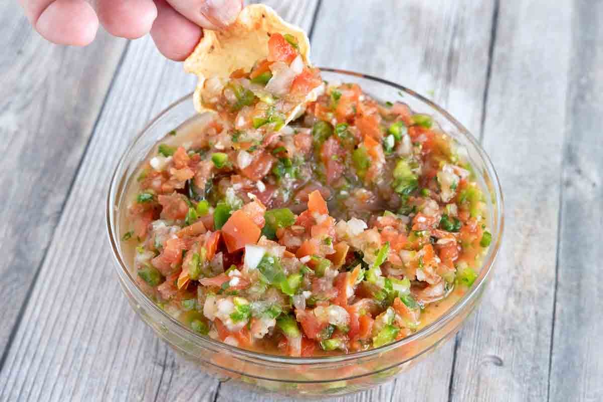 Hand reaching into the salsa fresca with a tortilla chip.
