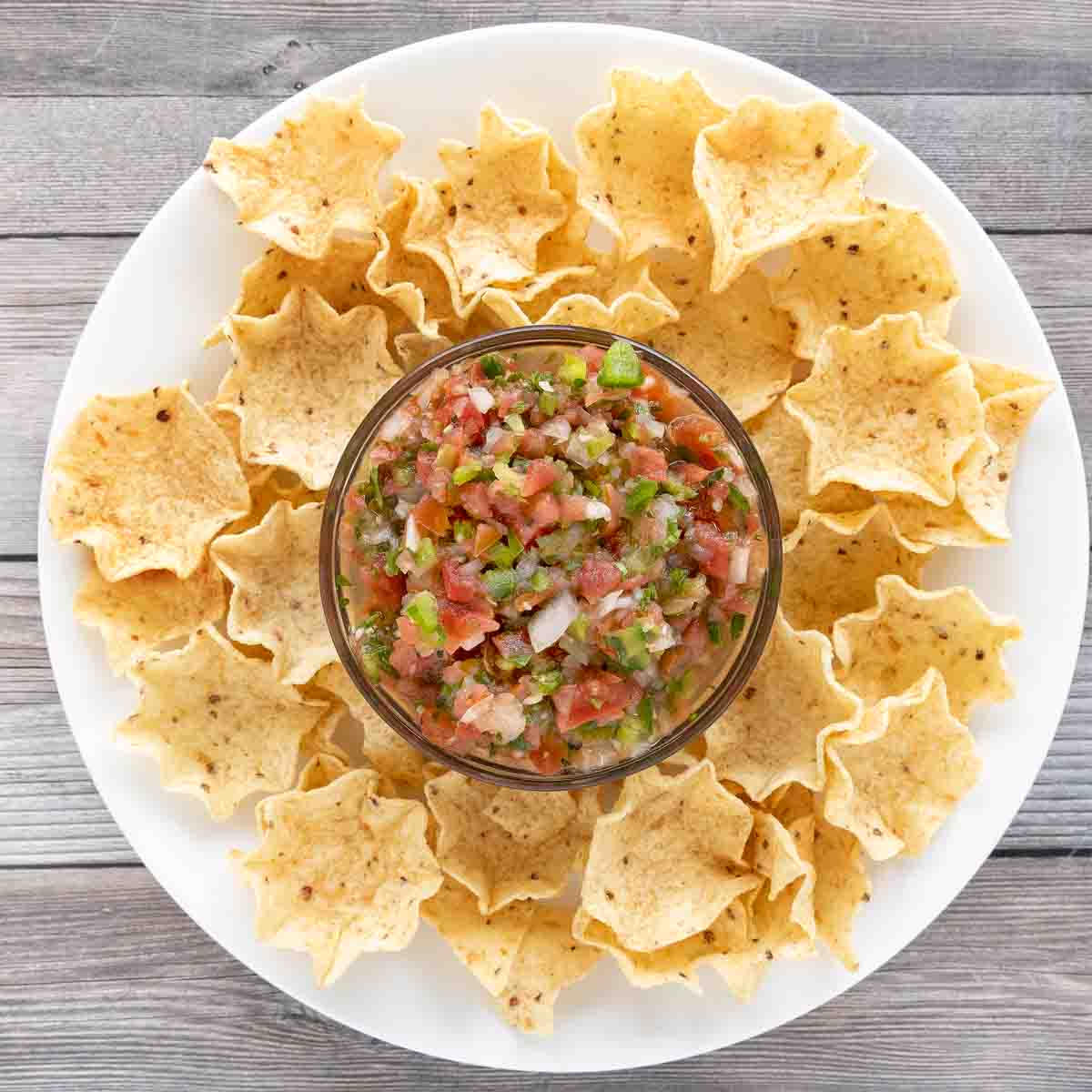Bowl of salsa fresca on a white plate surrounded by tortilla chips