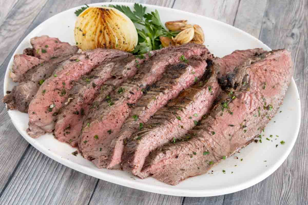 Sliced oven-baked tri-tip roast on a white platter.