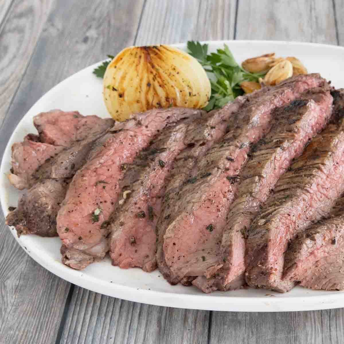 Sliced oven-baked tri-tip roast on a white platter.