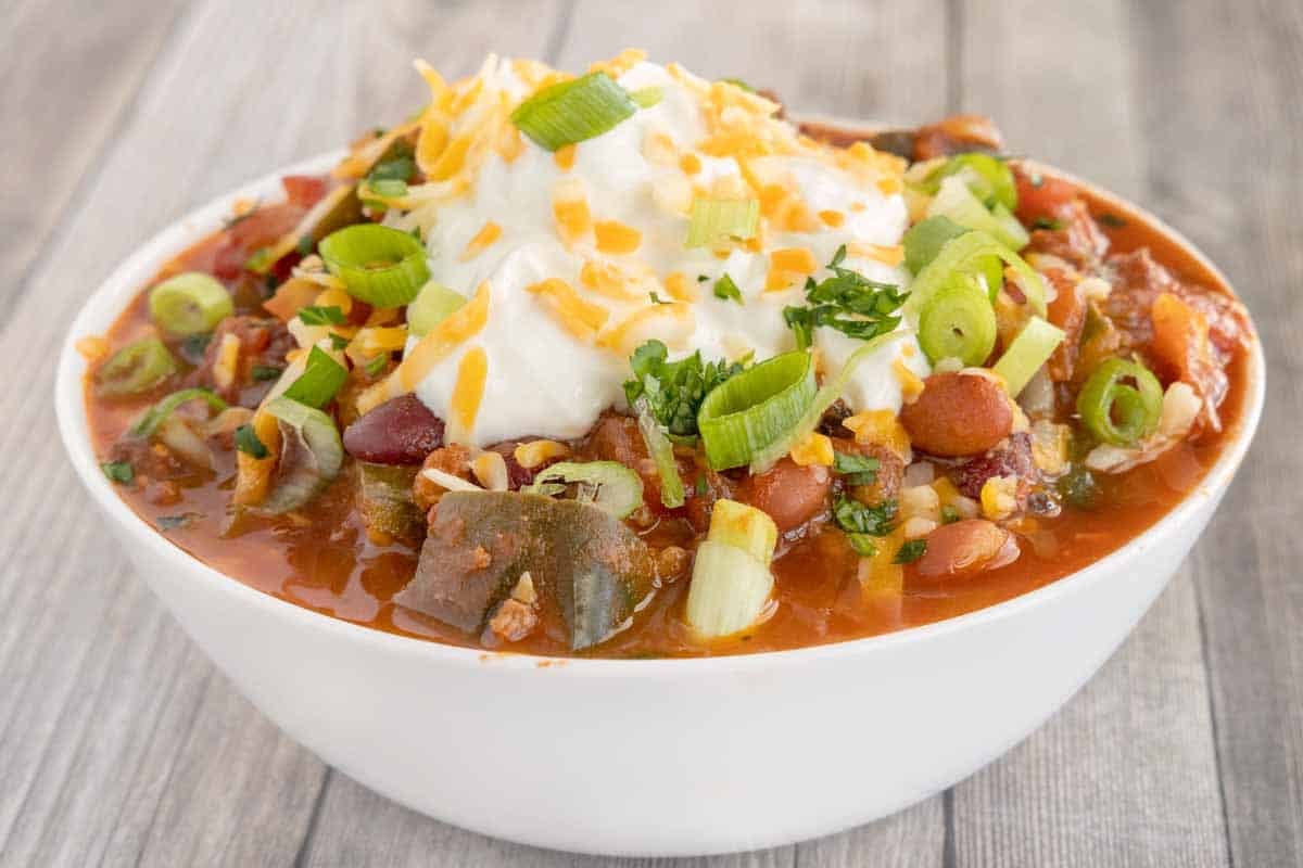 Venison chili topped with sour cream and shredded cheese in a white bowl.