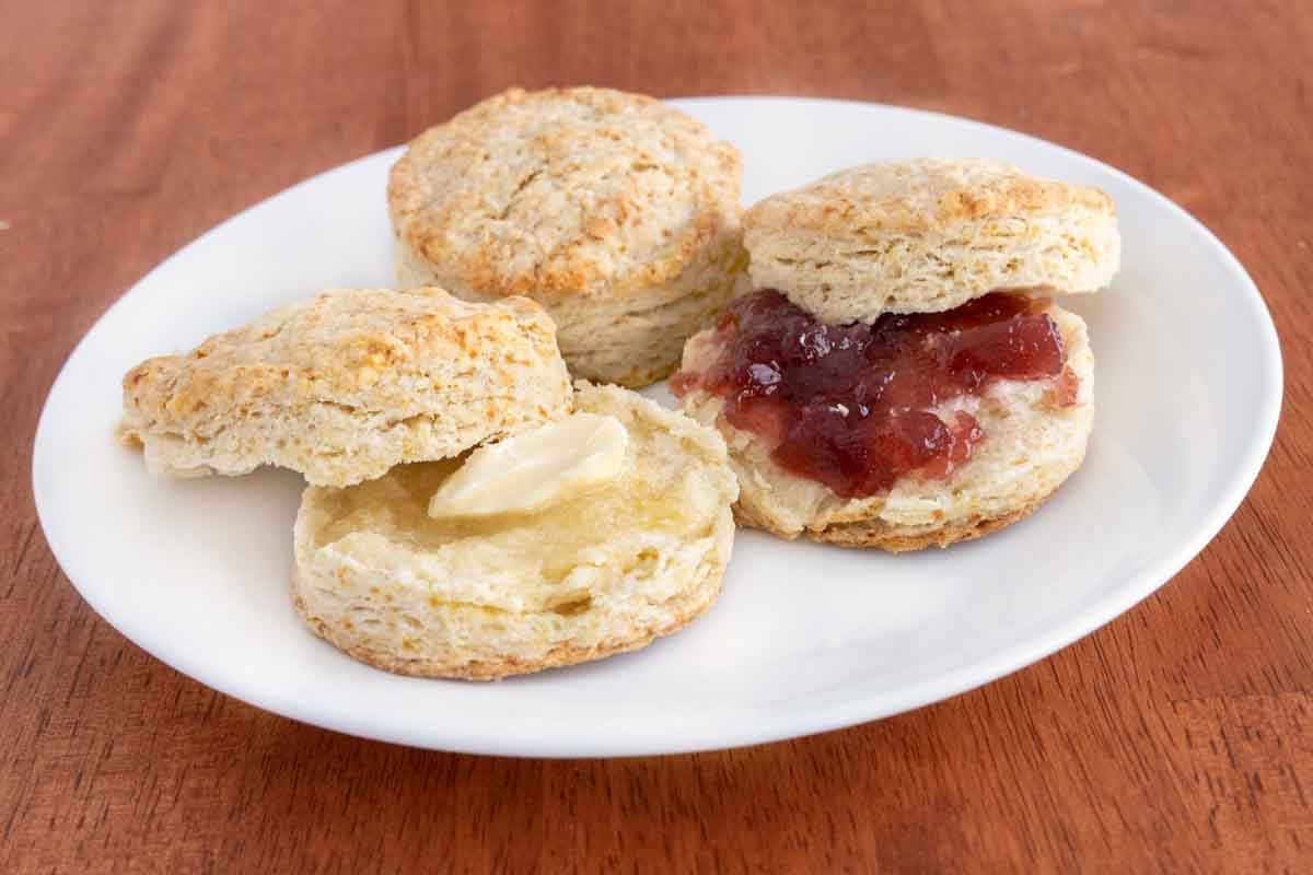 Homemade biscuits with butter and jam on a white plate.