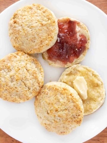 Homemade biscuits with butter and jam on a white plate.