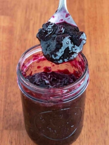 Blueberry jam in a glass jar with a spoon coming out.