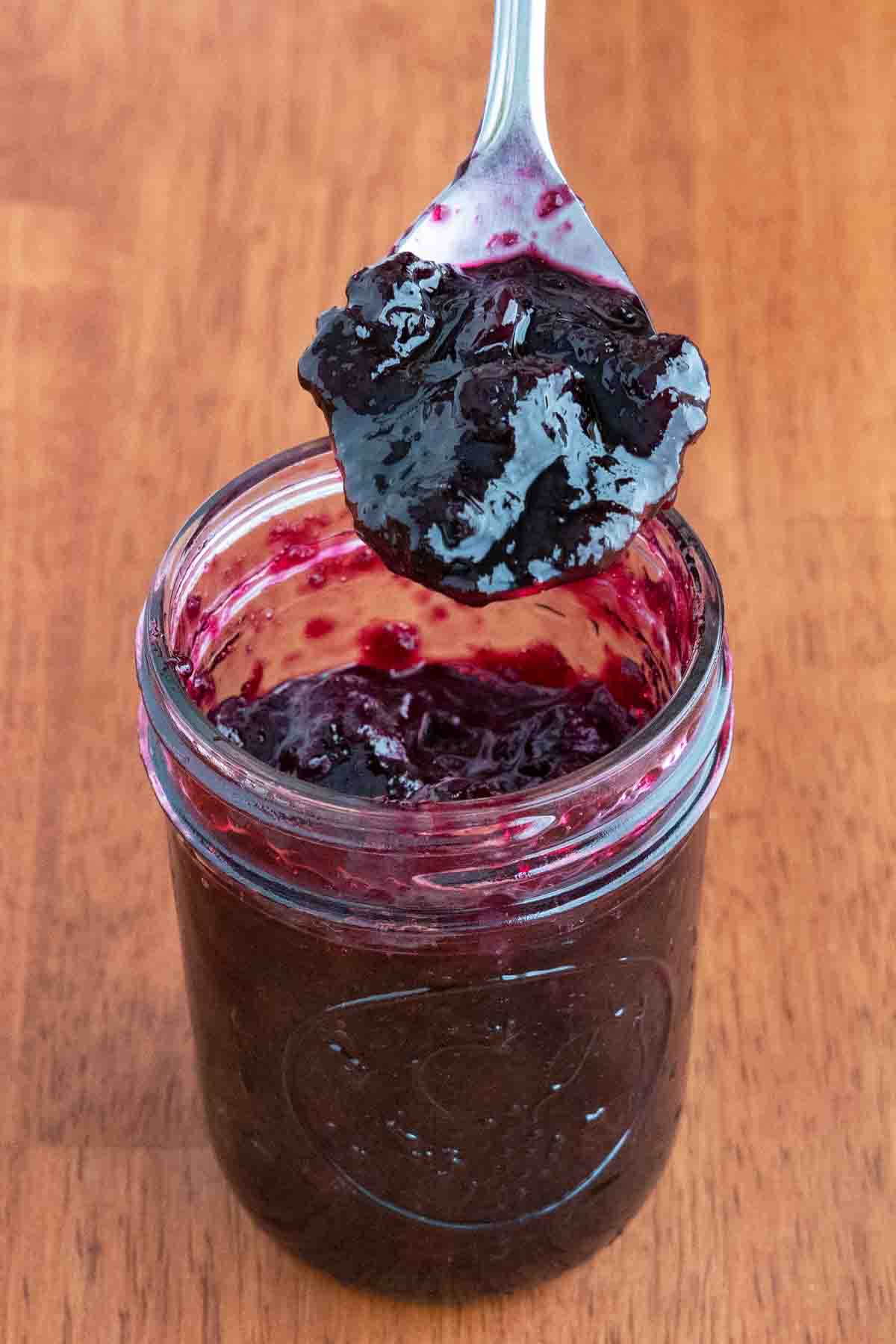 Blueberry jam in a glass jar with a spoon coming out.