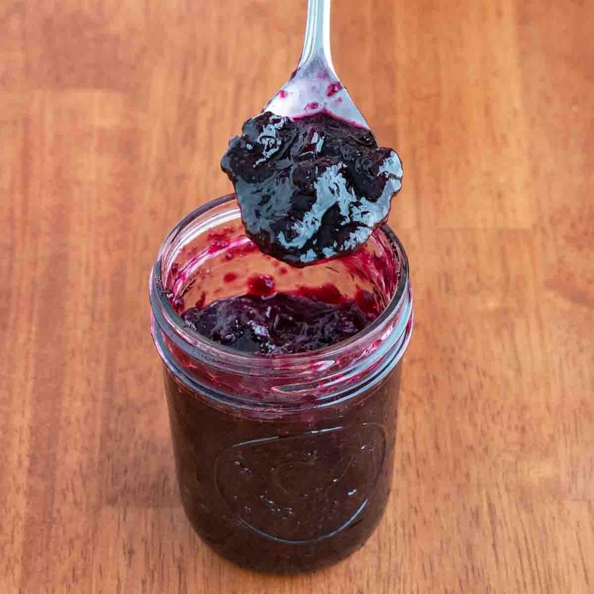 Blueberry jam in a glass jar with a spoon coming out.