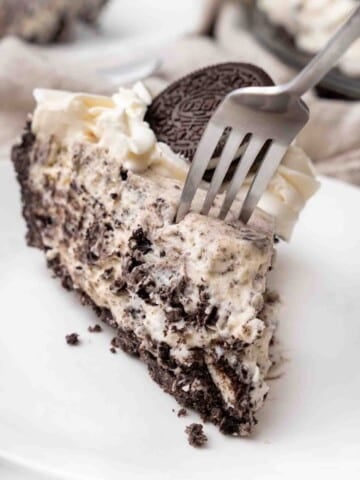Slice of an oreo pie with a fork in it on a white plate.