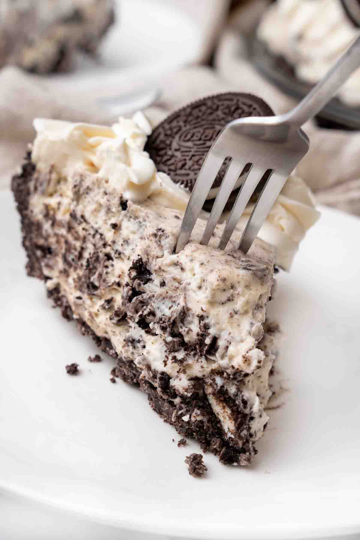 Slice of an oreo pie with a fork in it on a white plate.